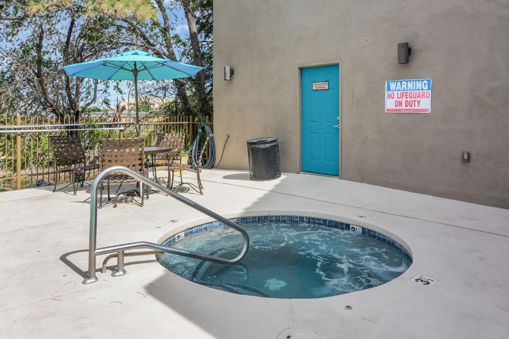 A hot tub sits in the middle of a patio with a warning sign on the wall.